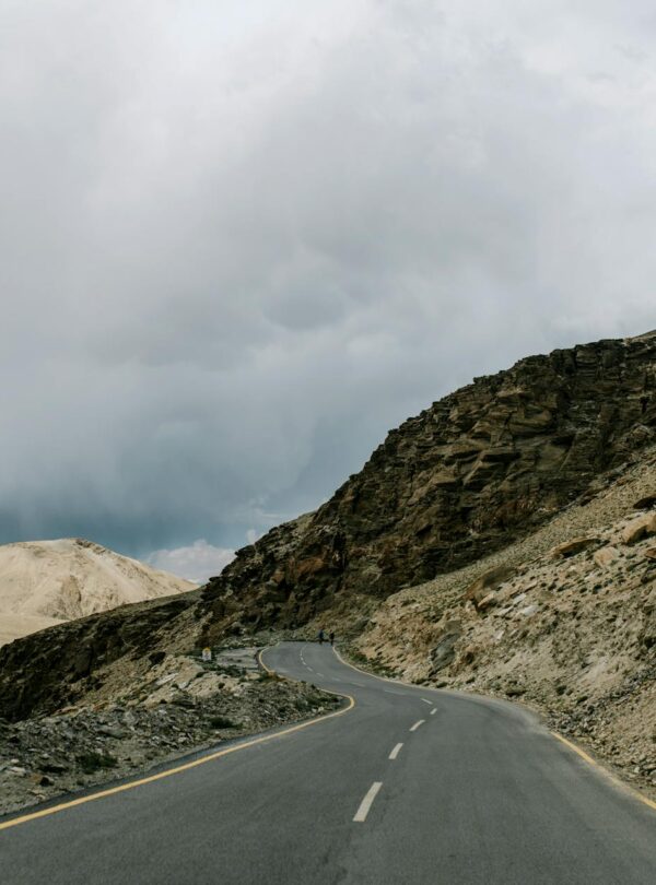 Winding mountain road to Ladakh with dramatic cloudy sky and rugged Himalayan landscape