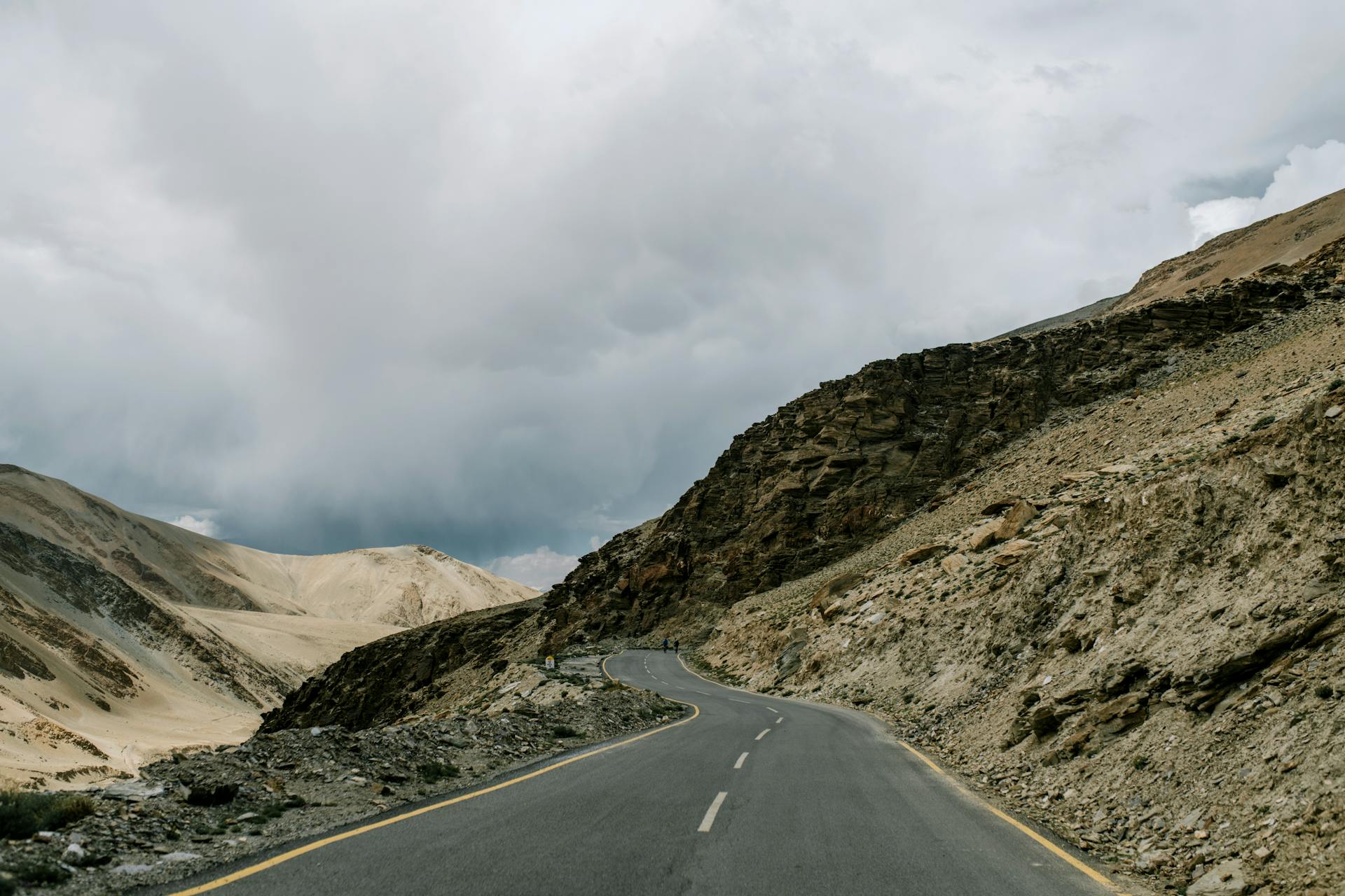 Winding mountain road to Ladakh with dramatic cloudy sky and rugged Himalayan landscape