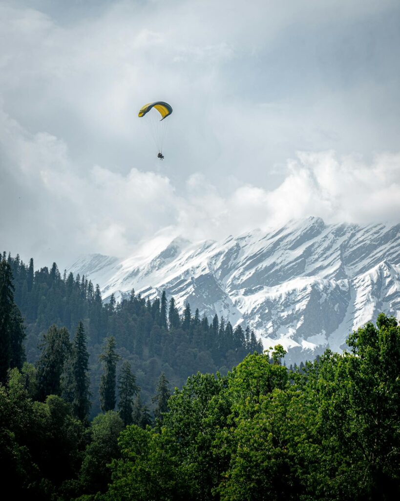 Paraglider flying over Solang Valley with snow-capped mountains in Manali, Himachal Pradesh