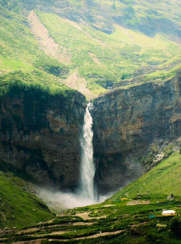 Sissu Waterfall cascading amidst lush greenery in Lahaul Valley near Manali, surrounded by snow-capped Himalayan mountains.