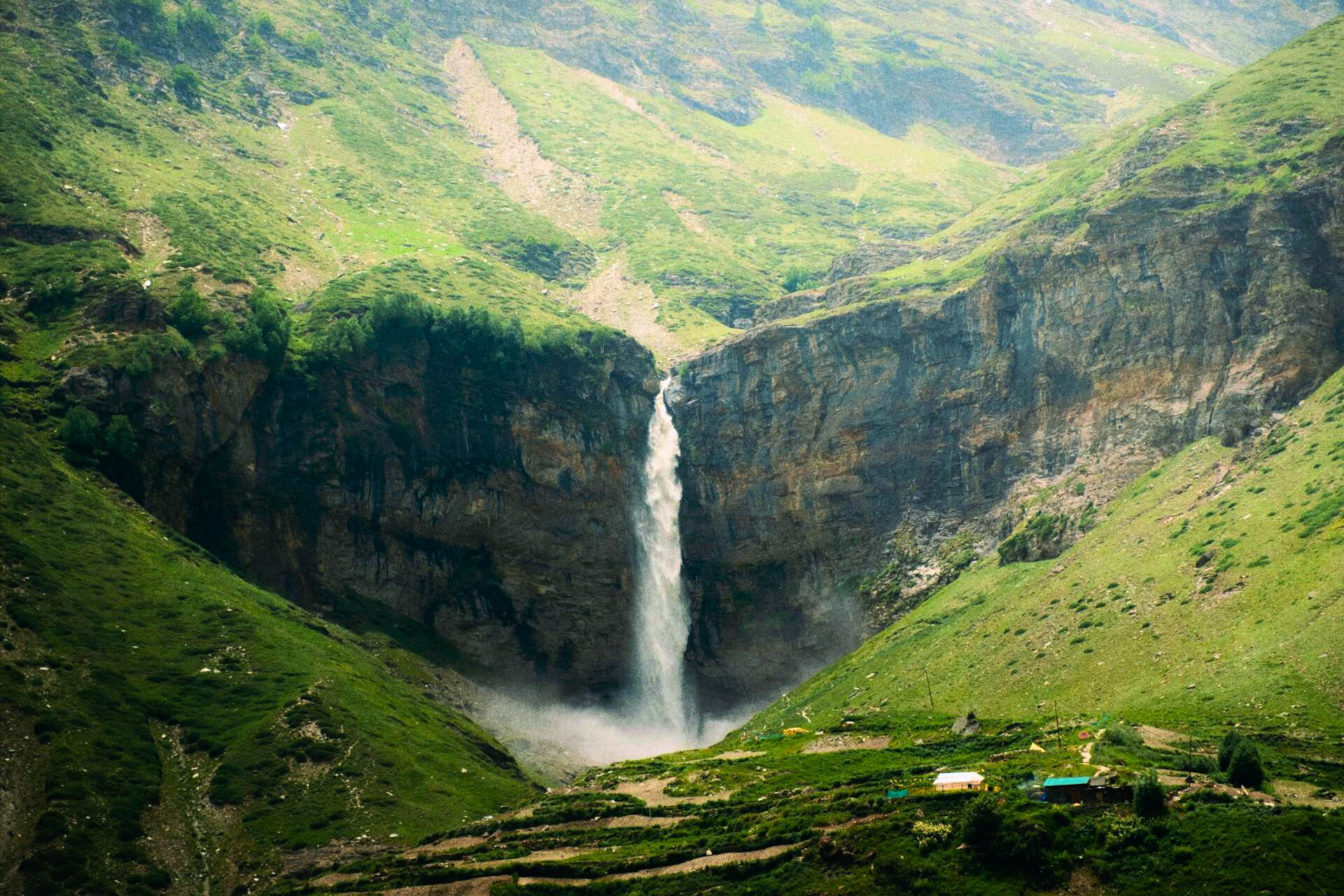 Sissu Waterfall cascading amidst lush greenery in Lahaul Valley near Manali, surrounded by snow-capped Himalayan mountains.